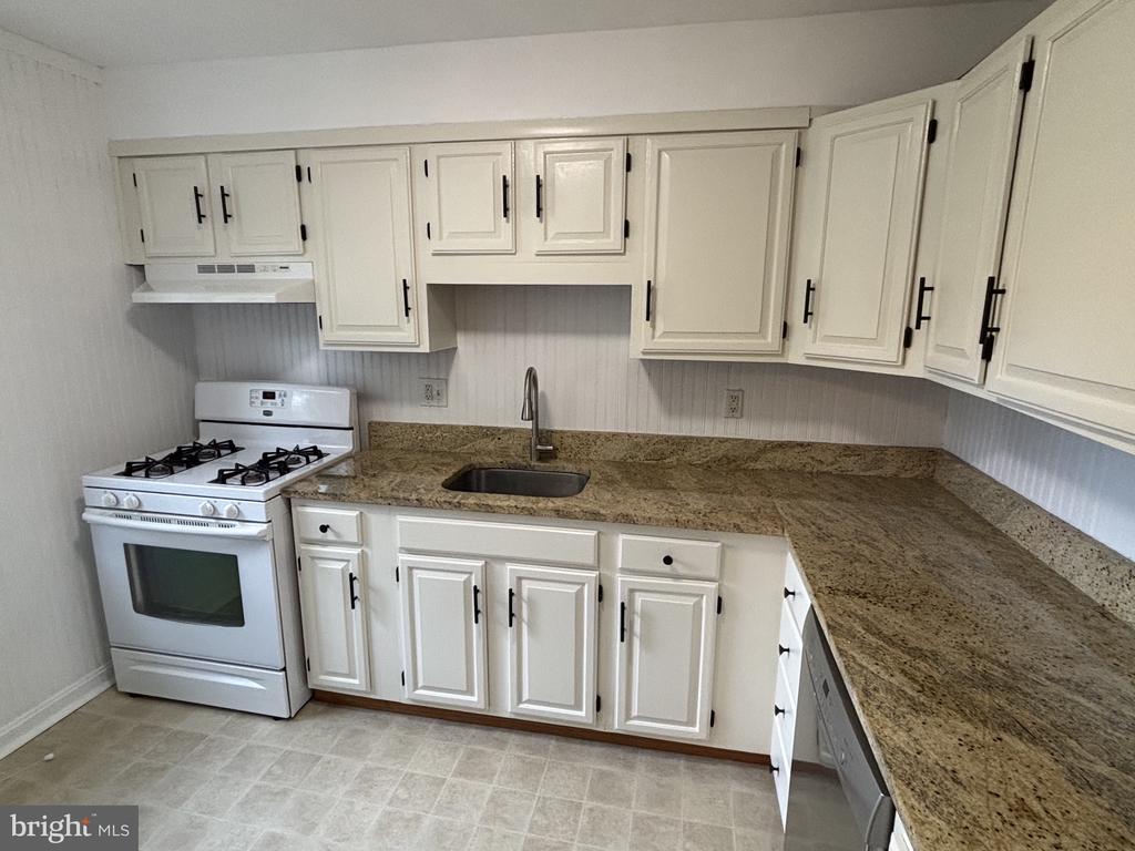 Kitchen with white cabinets, granite countertops, and a white gas range.