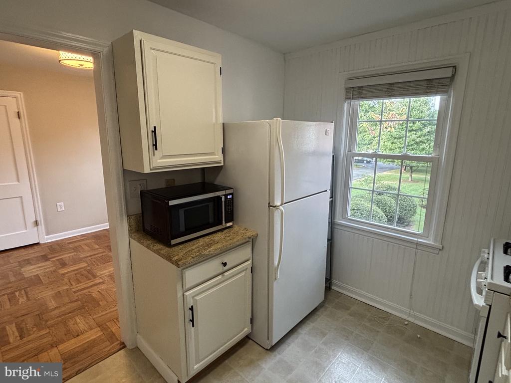 Kitchen with white cabinets, refrigerator, and microwave beside a window overlooking greenery.