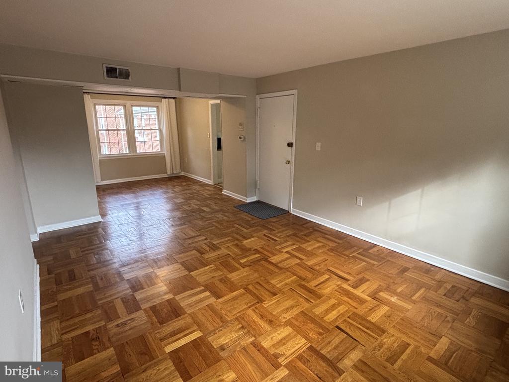 Empty living room with parquet flooring, a large window, and an entry door.