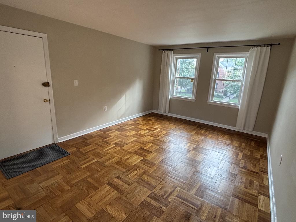 Empty room with parquet flooring and two curtained windows.