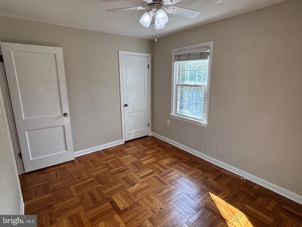 Empty room with patterned parquet flooring, a ceiling fan, and a sunlit window.