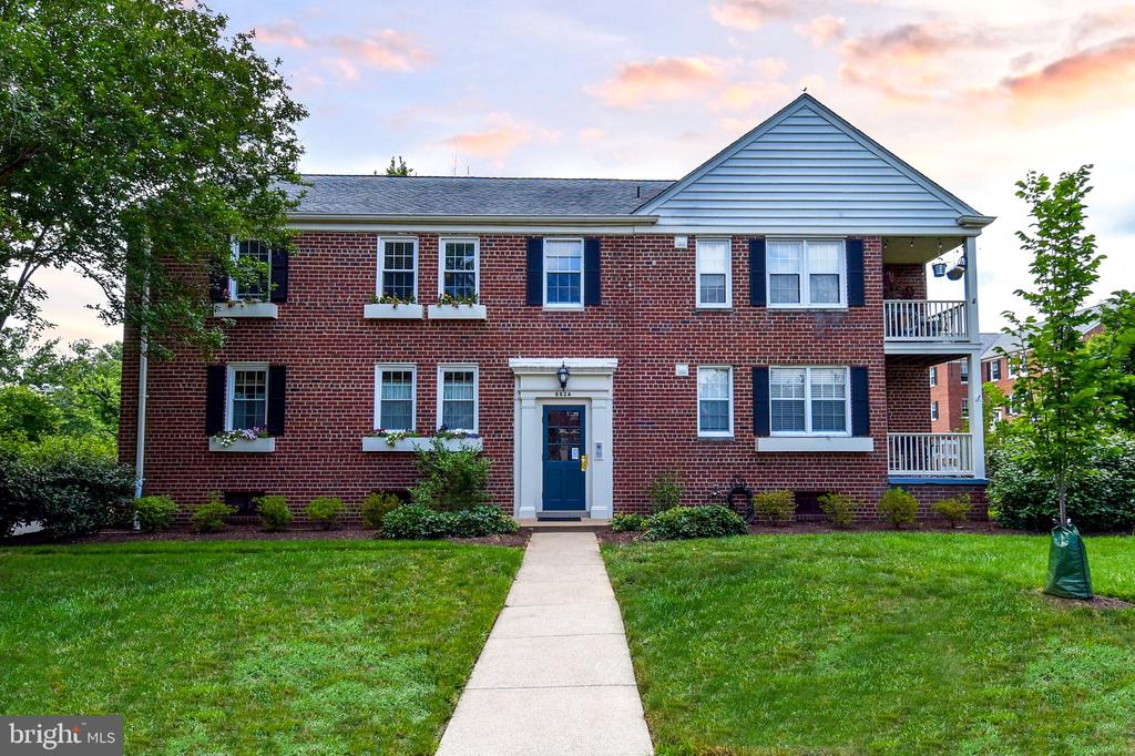 Two-story red-brick residential building with blue shutters and a walkway leading to the front door.