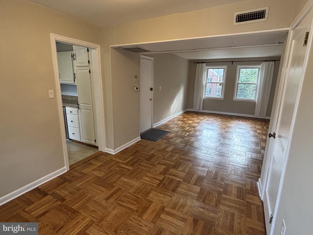 Vacant living and dining area with patterned parquet flooring and two curtained windows.