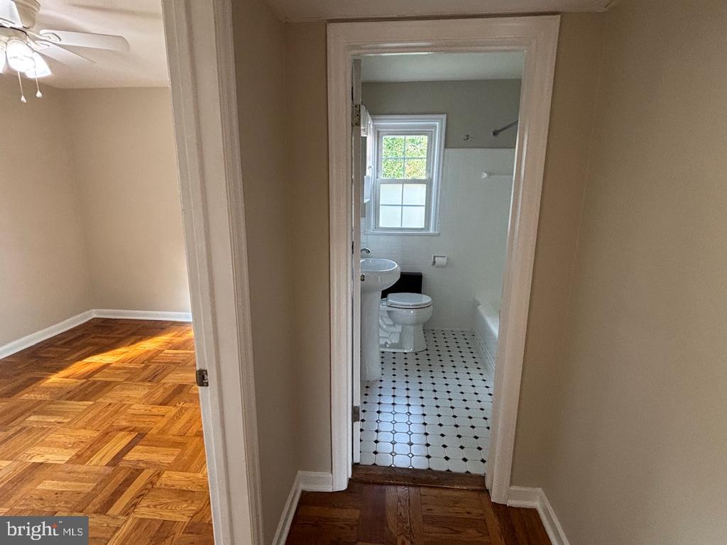 Hallway between an empty parquet-floored room and a bathroom with black-and-white tile.