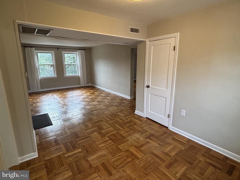 Vacant living area with parquet floors and two curtained windows.