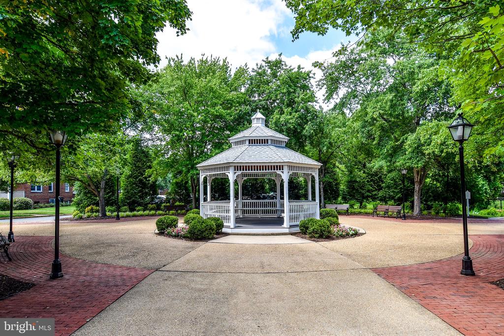 White gazebo in a leafy courtyard with benches and brick paving.