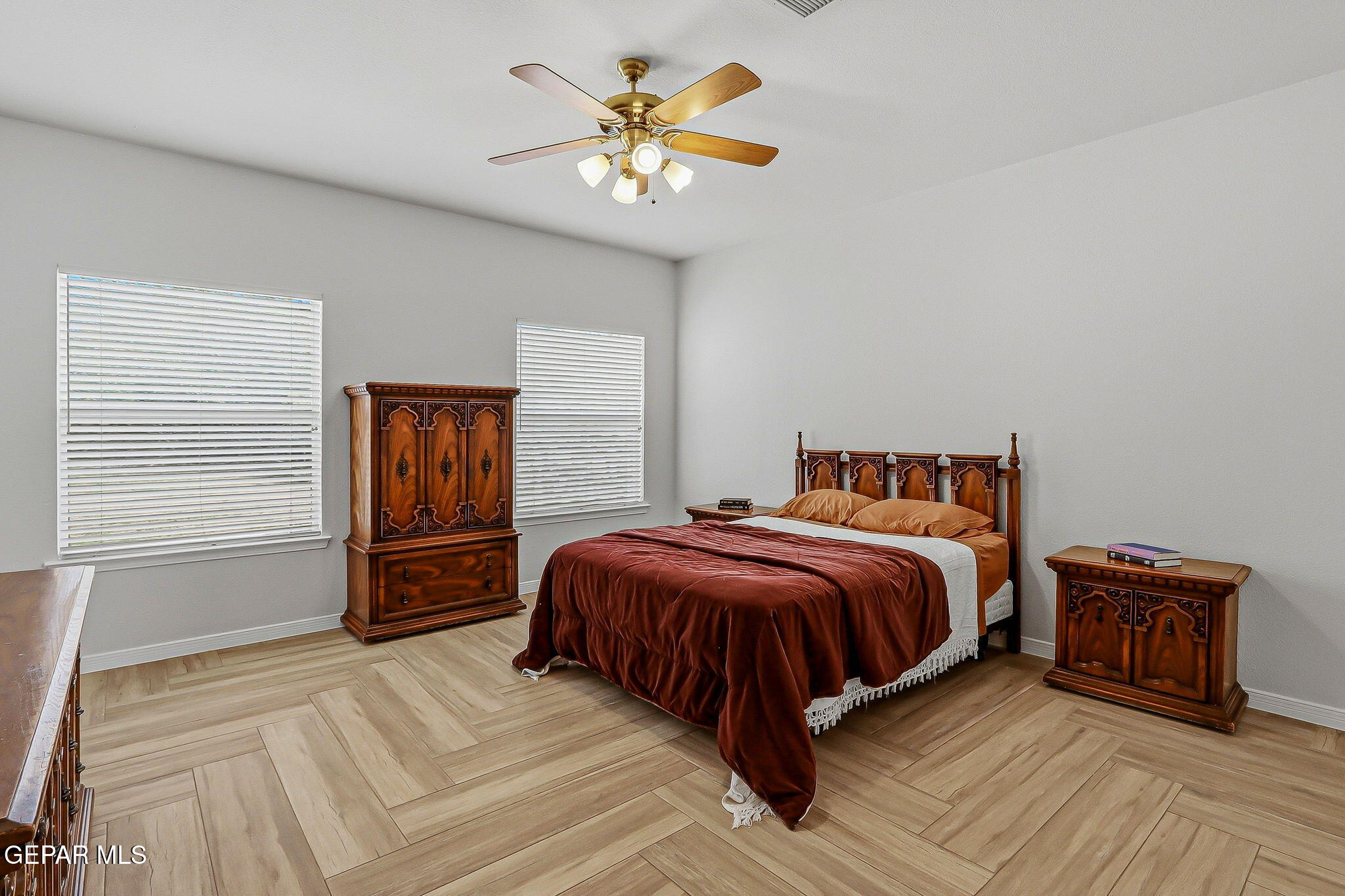 Bedroom with a burgundy-covered bed, ornate dark wood furniture, and light wood-look tile flooring.
