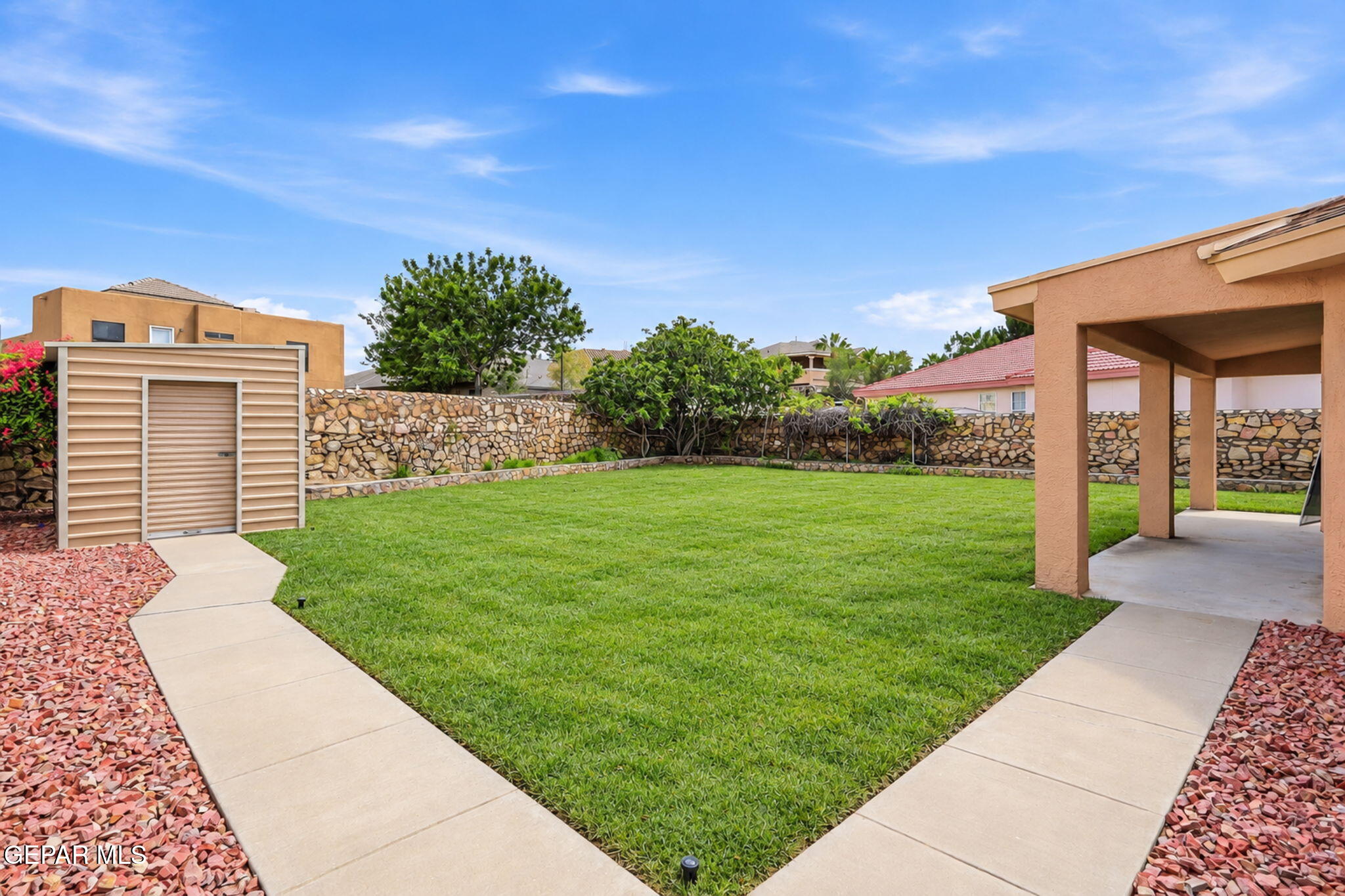 Backyard with a broad lawn, curved walkways, covered patio, and small storage shed.