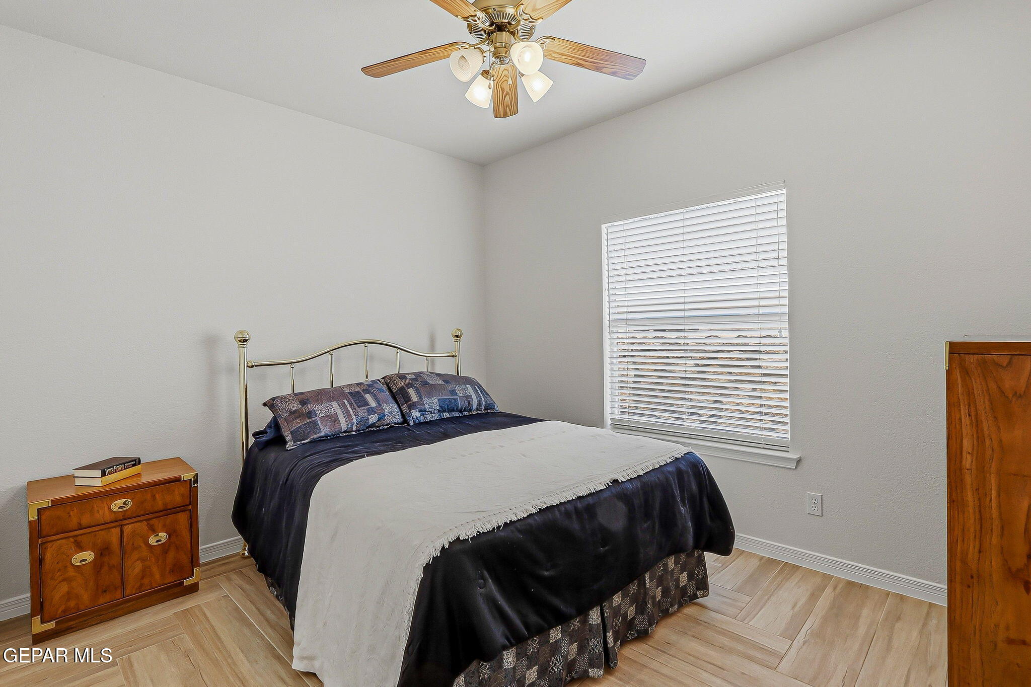Furnished bedroom with a brass bed, navy bedding, wood nightstand, and window with white blinds.