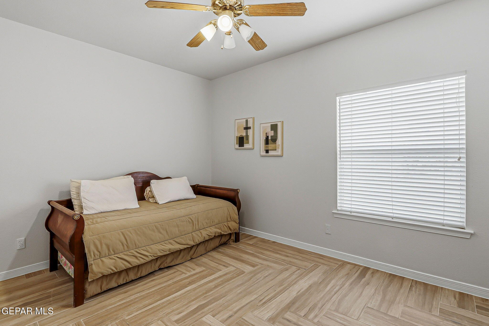 Bedroom with a tan-covered dark wood daybed, wood-look tile flooring, and a large window with white blinds.