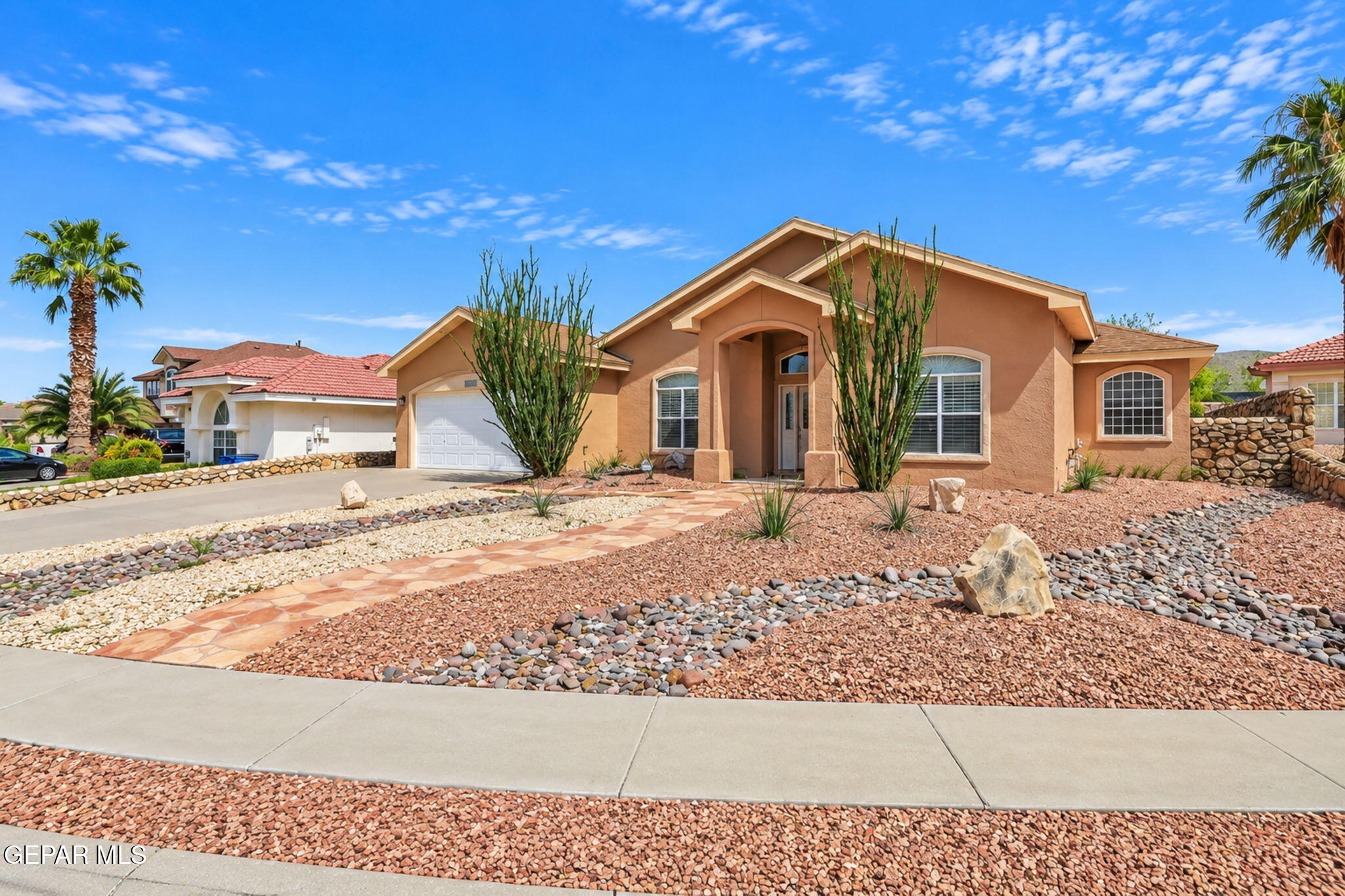 Single-story tan stucco home with an arched entry and desert rock landscaping.