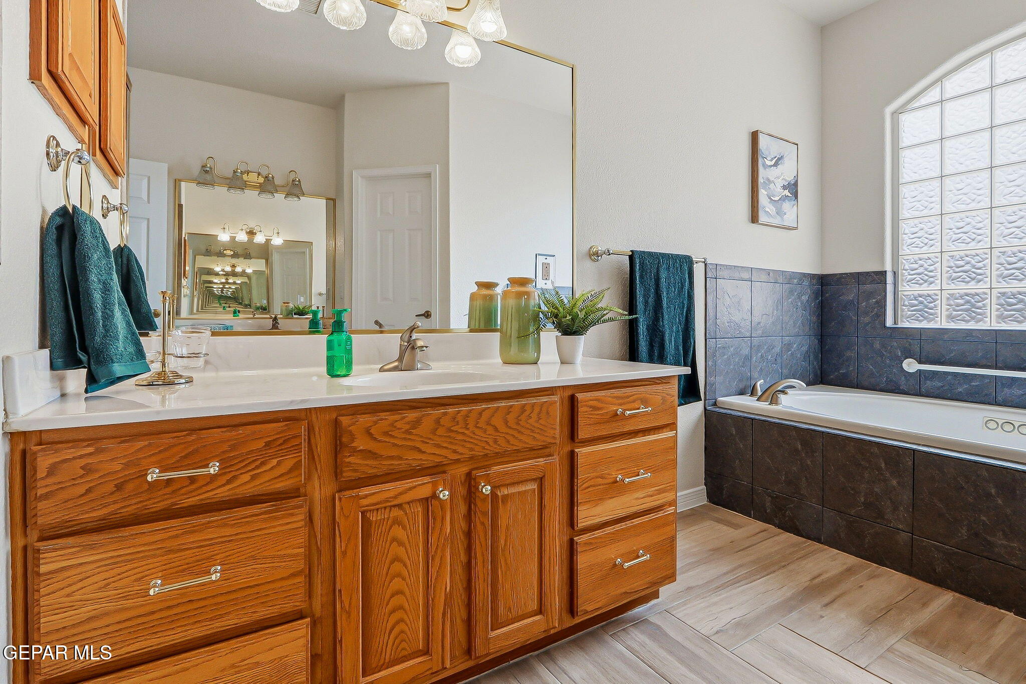 Bathroom with a wood vanity and bathtub beneath a glass-block window.