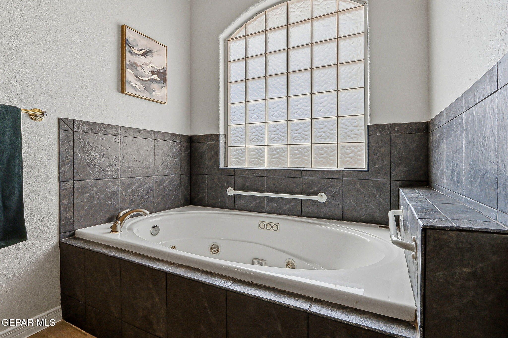 Bathroom with a jetted tub, dark tile surround, and large arched glass-block window.