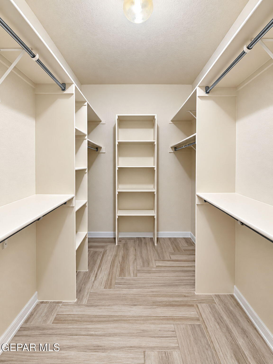 Walk-in closet with built-in shelving, hanging rods, and wood-look tile flooring.