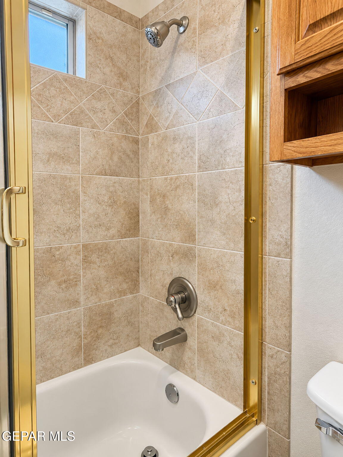 Bathroom tub and shower with beige tile, glass enclosure, and wooden cabinet.
