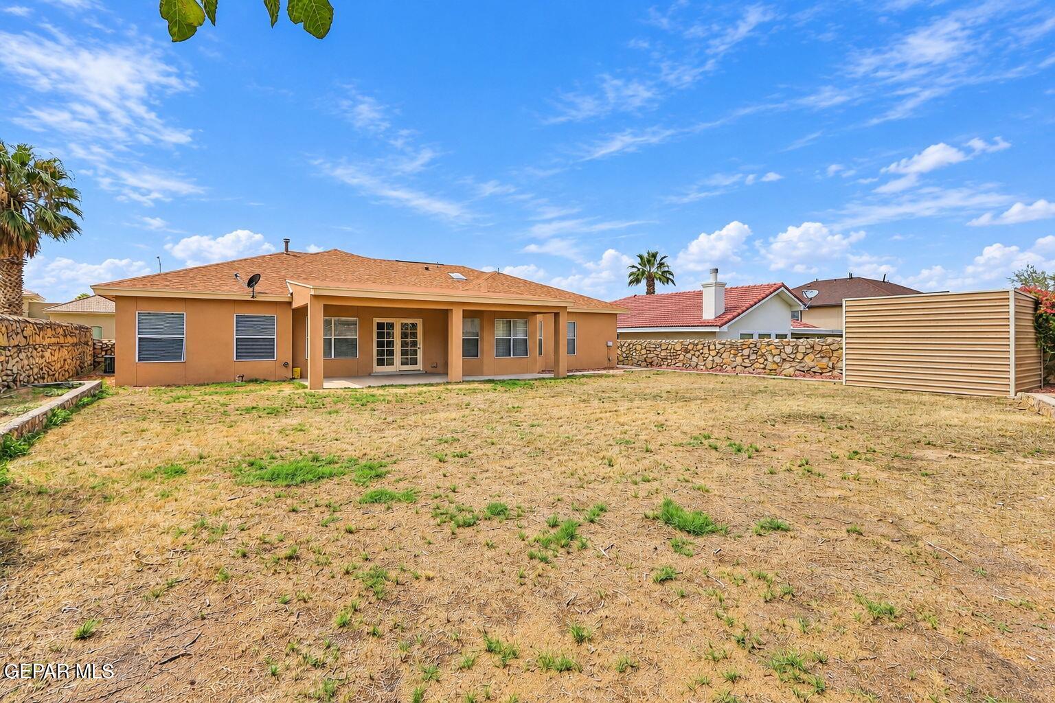 Rear of a tan single-story home with a covered patio and a large, dry backyard.