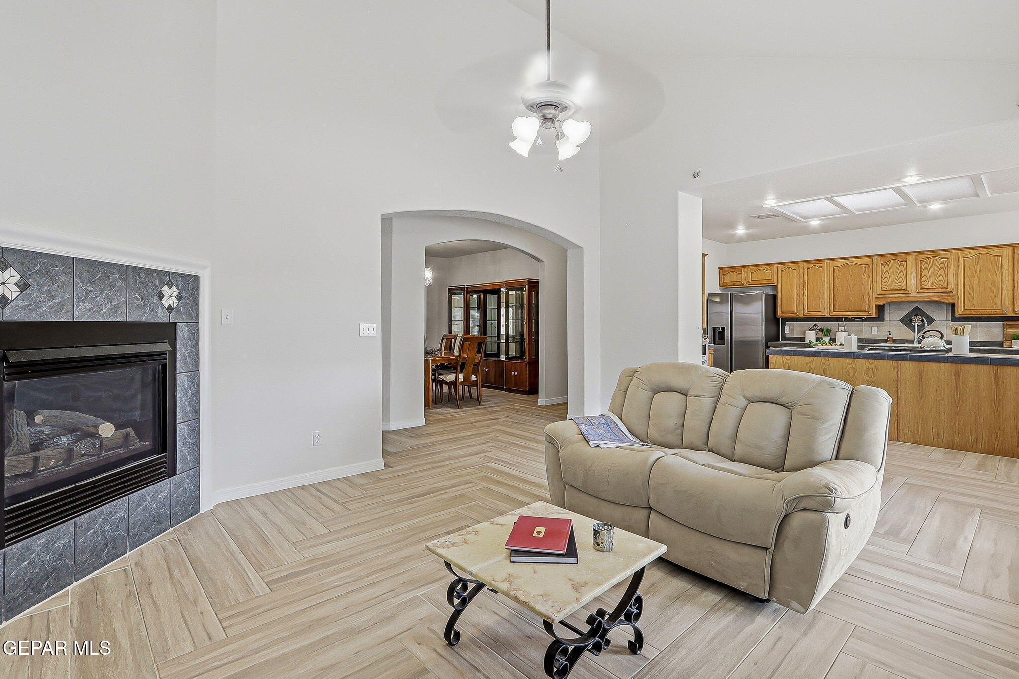 Living room with a stone-faced fireplace, beige reclining sofa, and open kitchen.