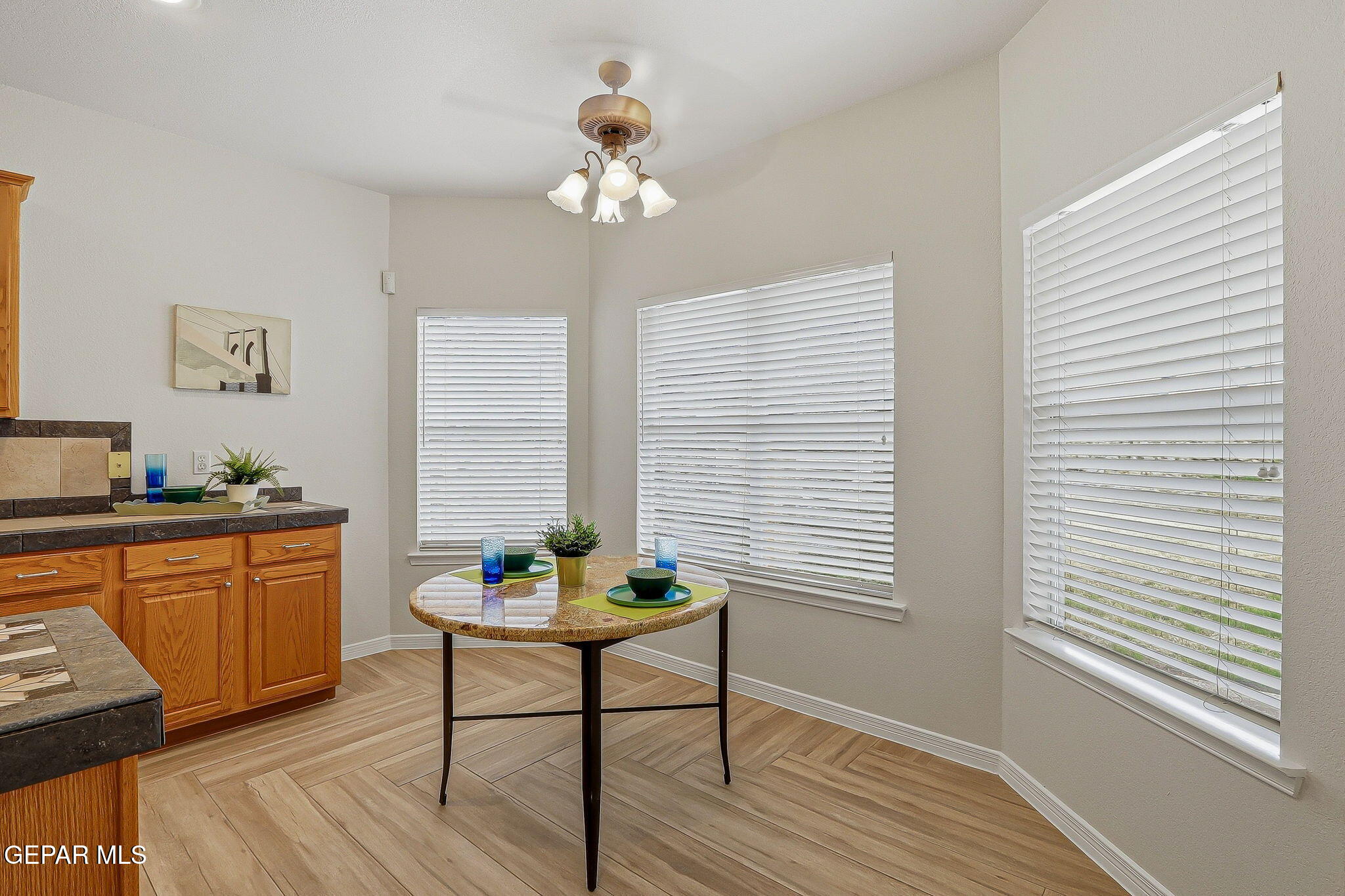 Kitchen breakfast nook with a round set table, wood cabinetry, and three windows with white blinds.