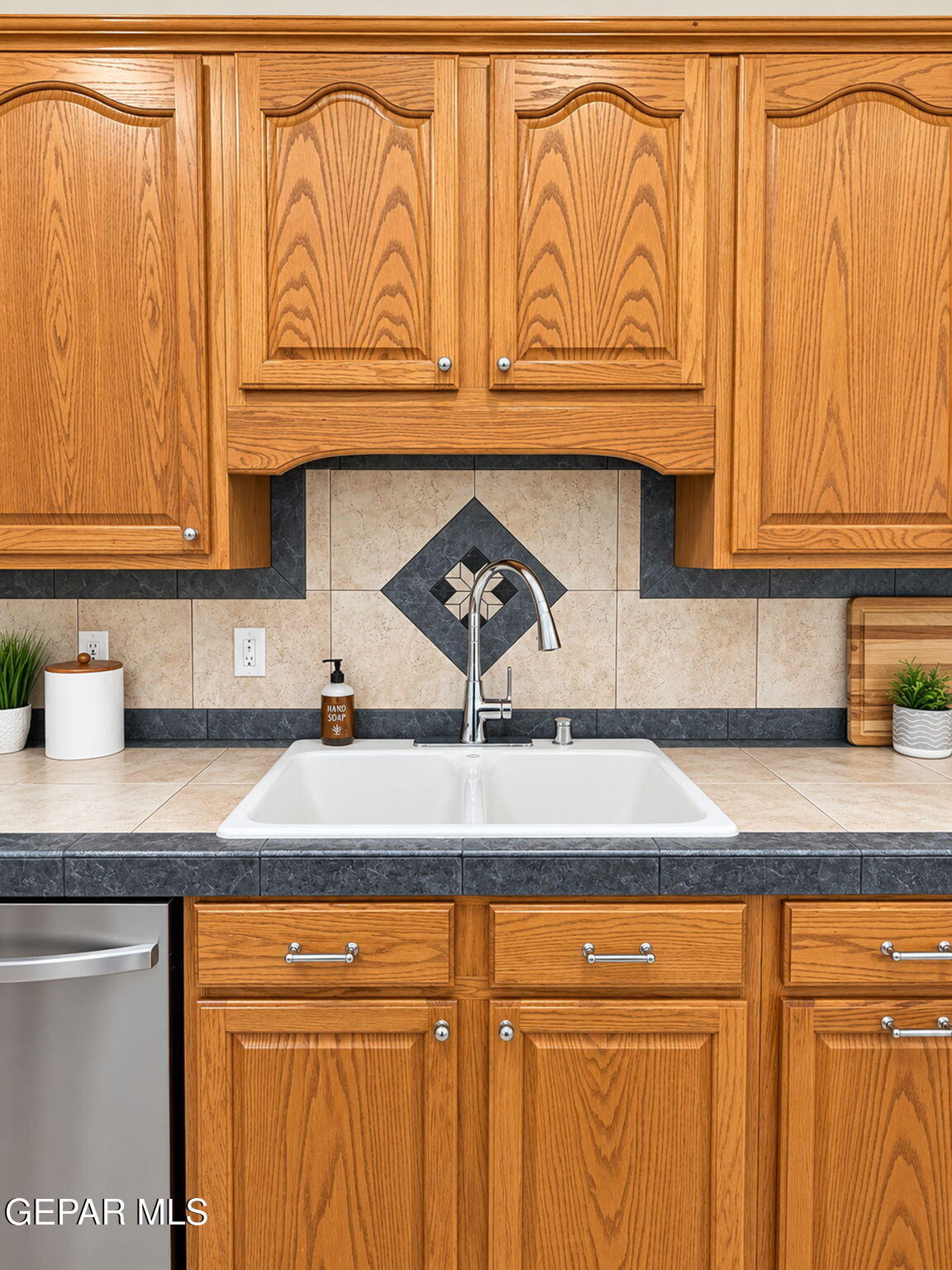 Kitchen sink beneath oak cabinets, with a tiled backsplash and stainless steel dishwasher.