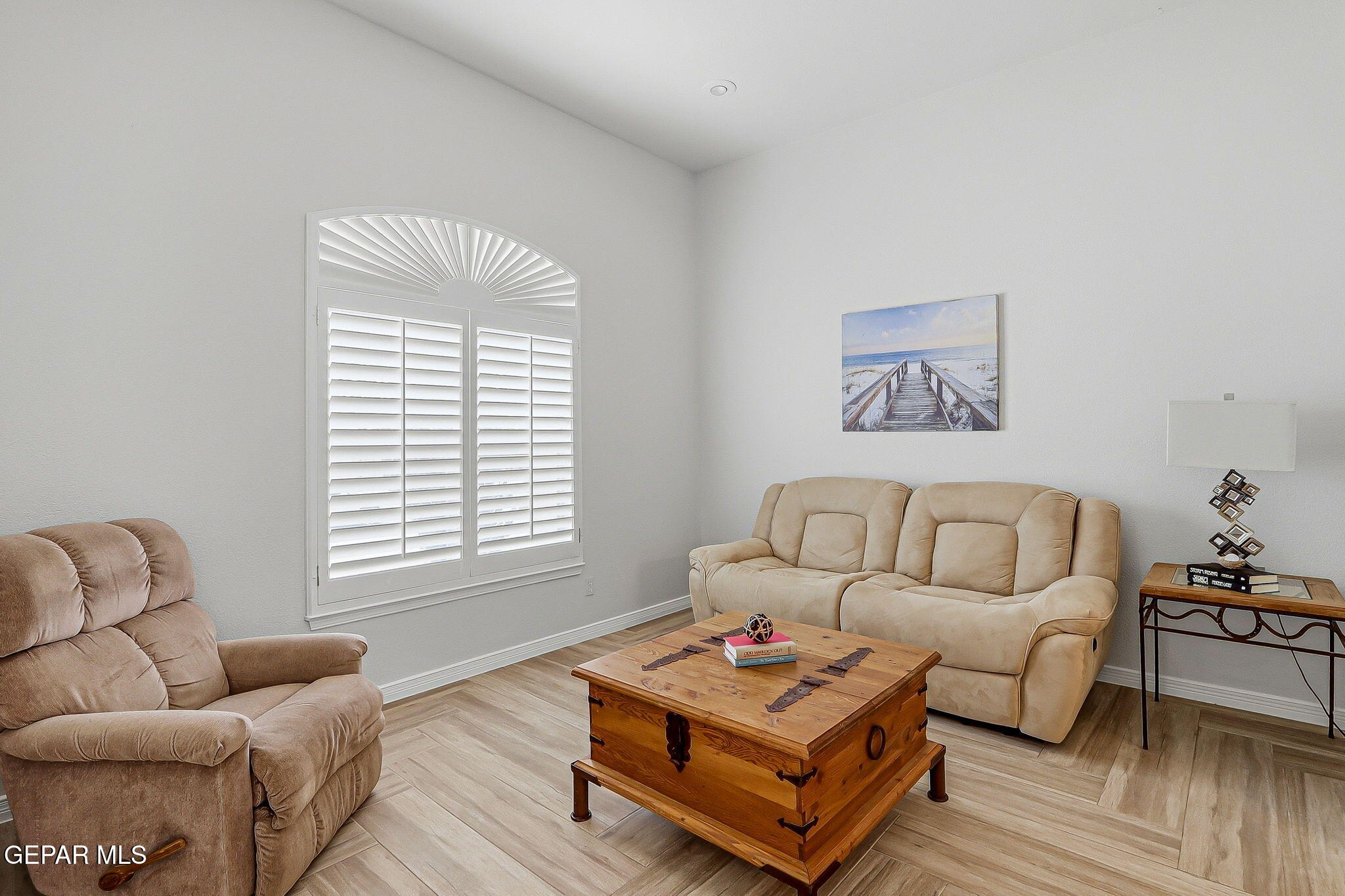 Living room with beige recliners, a wooden trunk coffee table, and a large shuttered window.