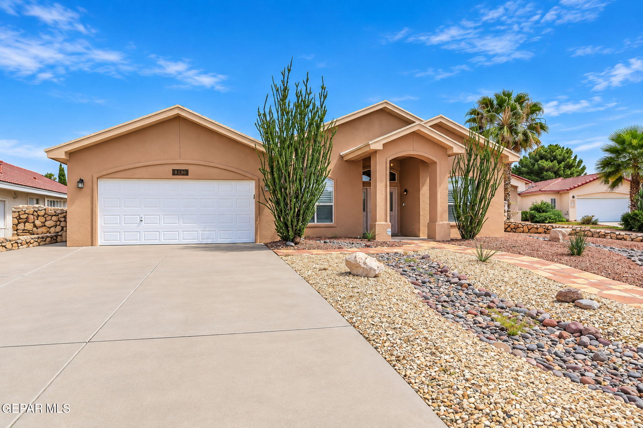 Tan stucco house with a white garage, arched entry, and desert rock landscaping.