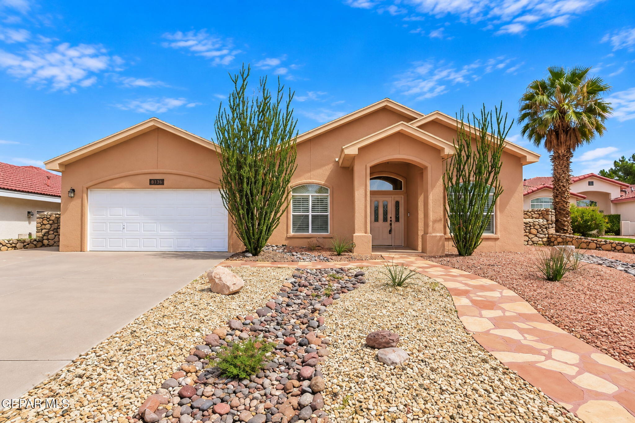 Peach stucco home with an attached garage, arched entry, and rock-and-gravel desert landscaping.