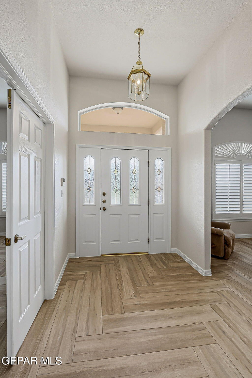 Entry foyer with a white decorative-glass front door, brass lantern, and wood-look tile flooring.