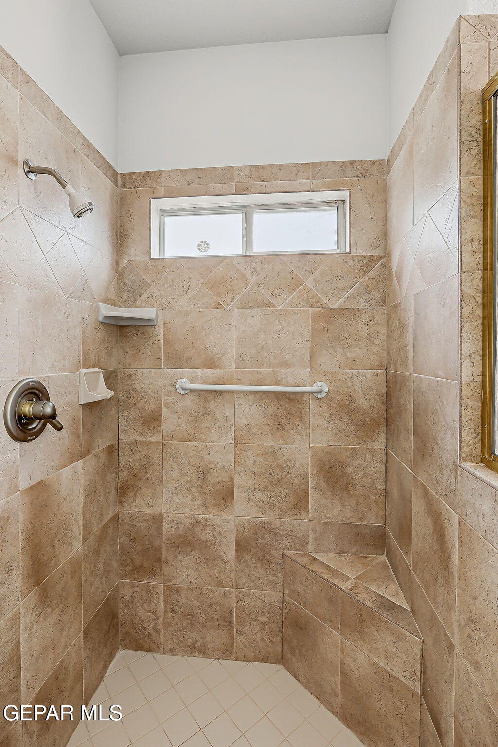 Tiled walk-in shower with built-in bench, grab bar, and high horizontal window.