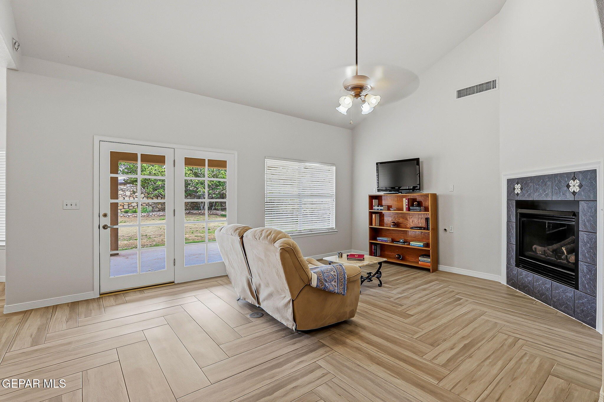 Living room with French patio doors, a tiled fireplace, and light wood-look tile flooring.