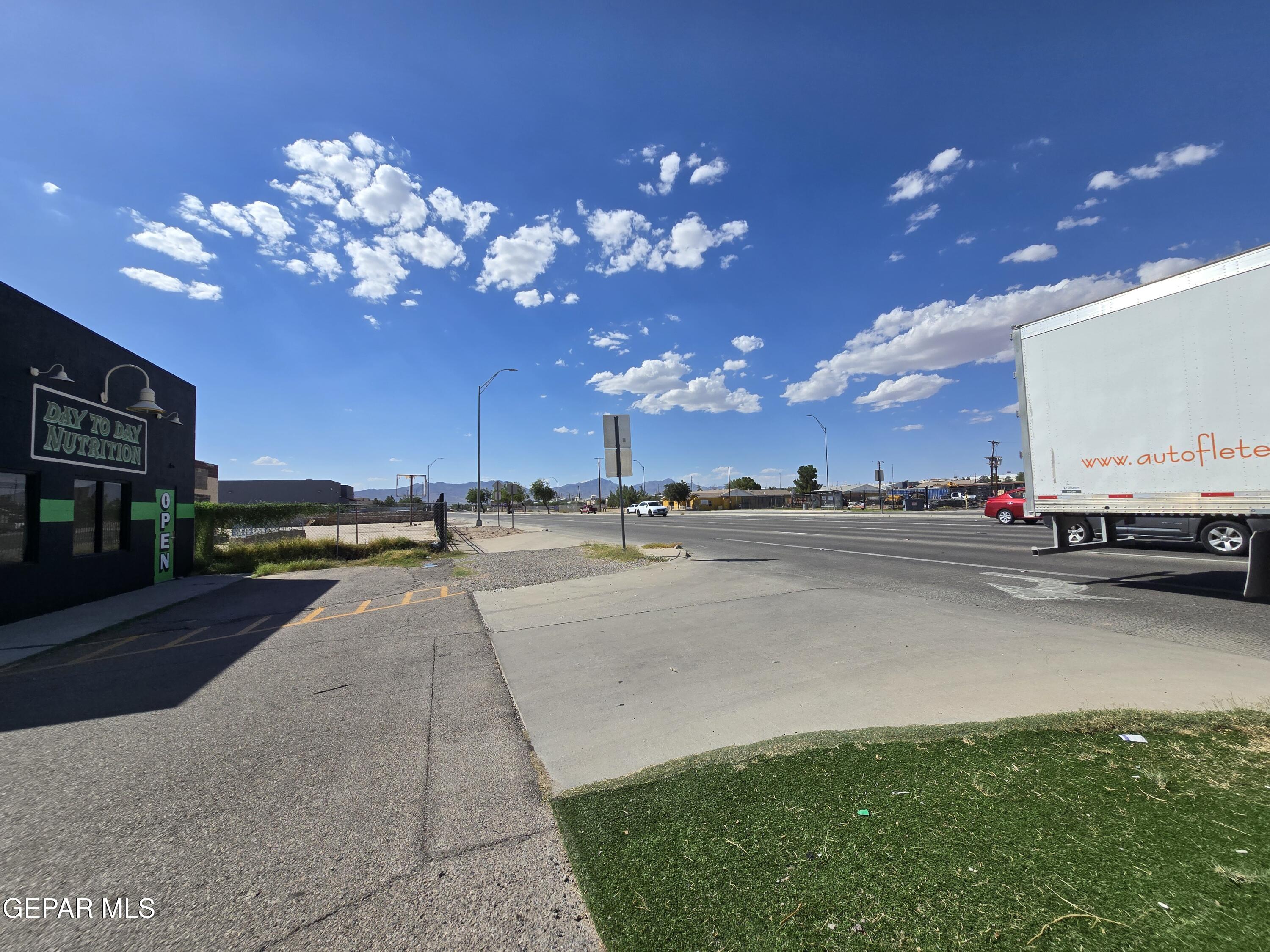 Commercial property frontage beside a busy road, with a neighboring business and distant mountains.