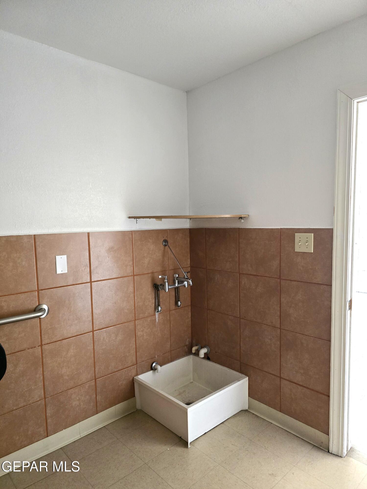 Tiled utility area with a deep white wash basin and wall-mounted faucet.