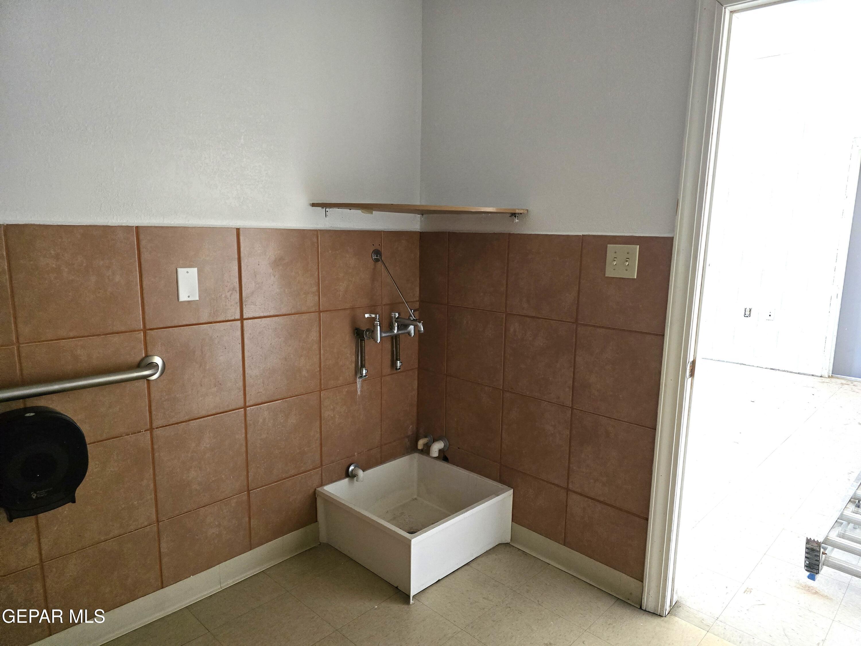 Tiled utility wash area with a deep white basin and wall-mounted faucet.