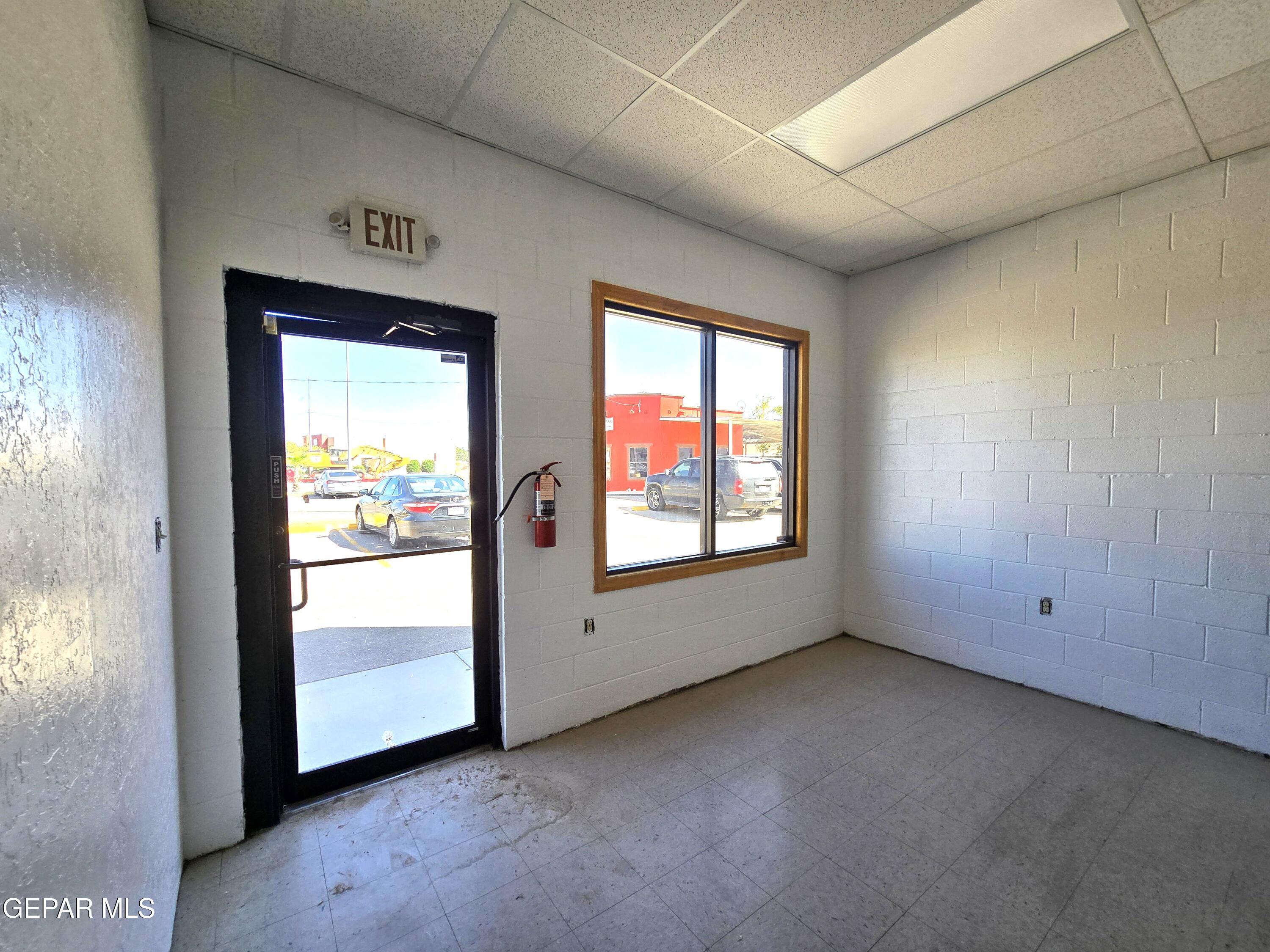 Vacant commercial entry room with tiled floor, glass exit door, and wood-trimmed window.