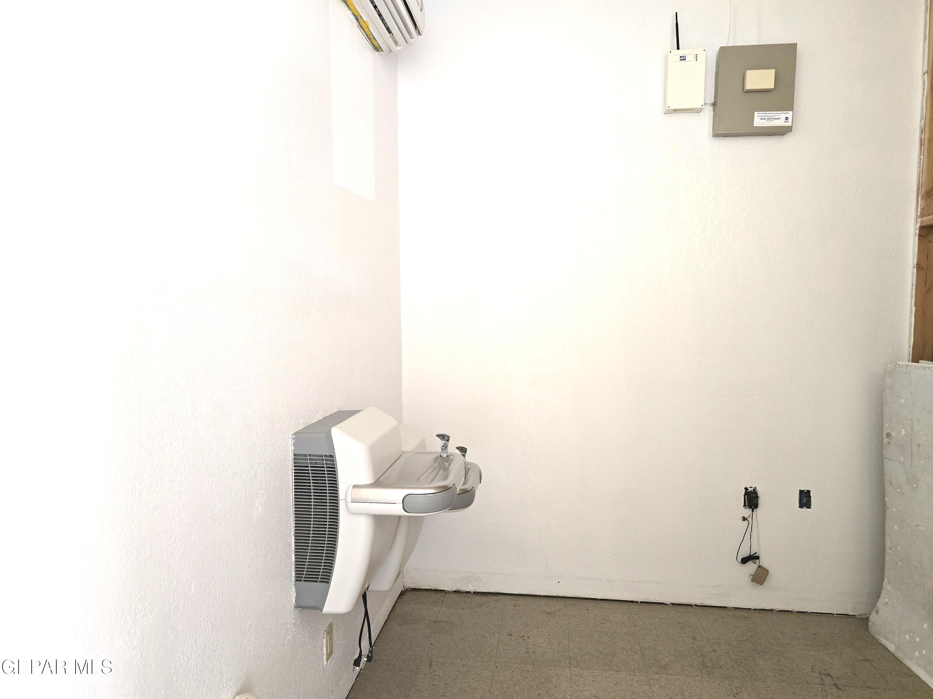 Vacant room with a wall-mounted drinking fountain and security equipment.