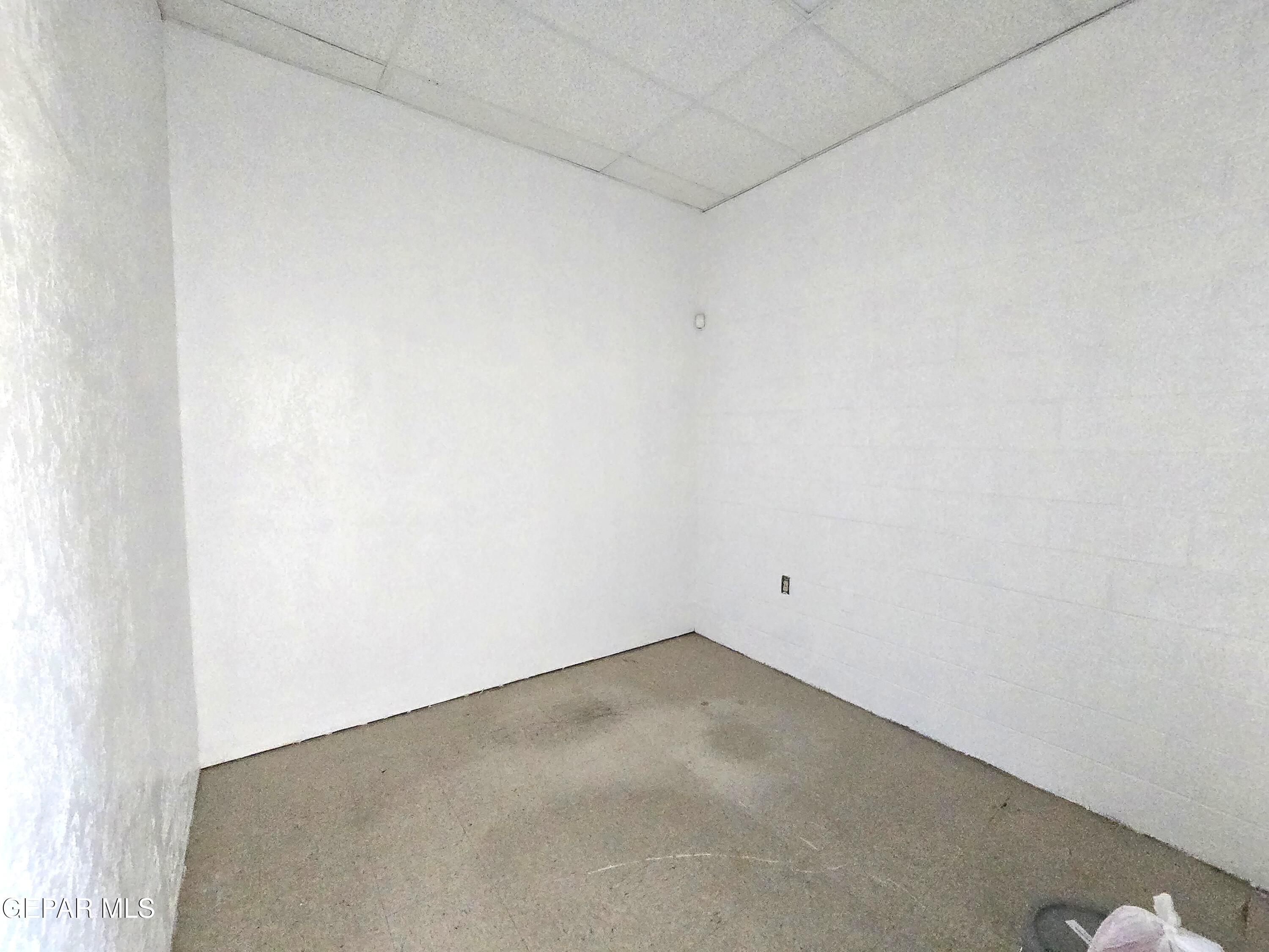 Empty room with white walls, gray concrete floor, and suspended ceiling.