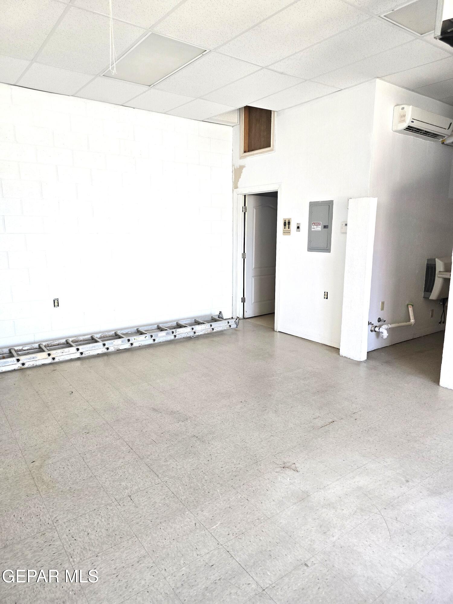 Vacant commercial interior with tiled flooring, a ladder along the wall, and an open doorway beside a utility area.