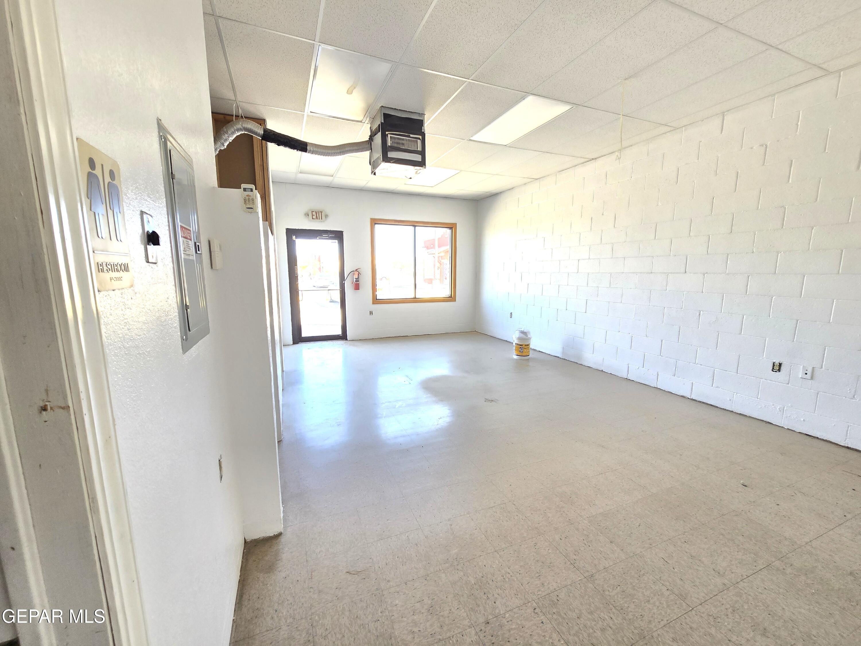 Vacant commercial room with white block walls, tiled floor, and a front window and door.