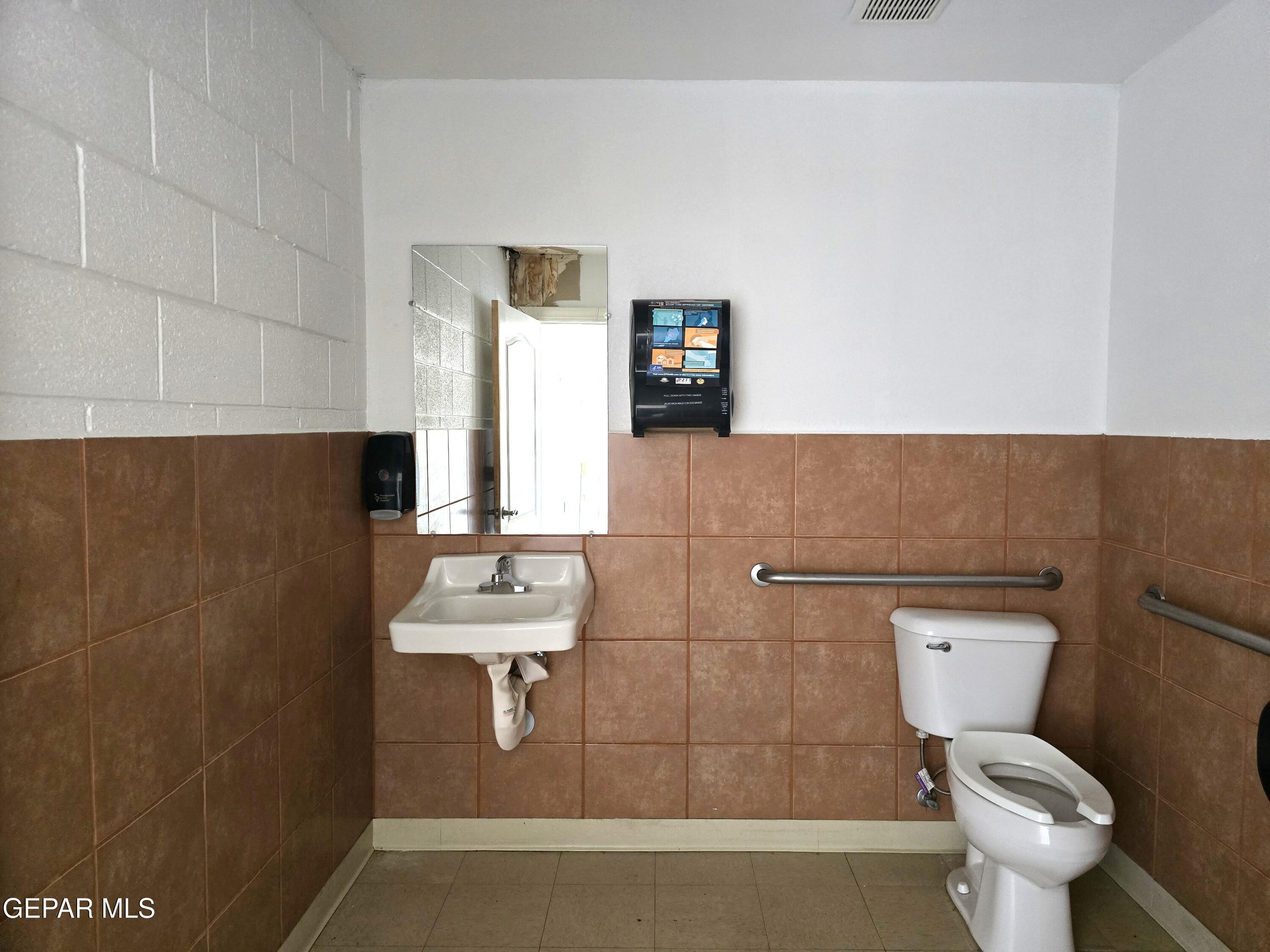 Accessible bathroom with brown tile, wall-mounted sink, toilet, and grab bars.