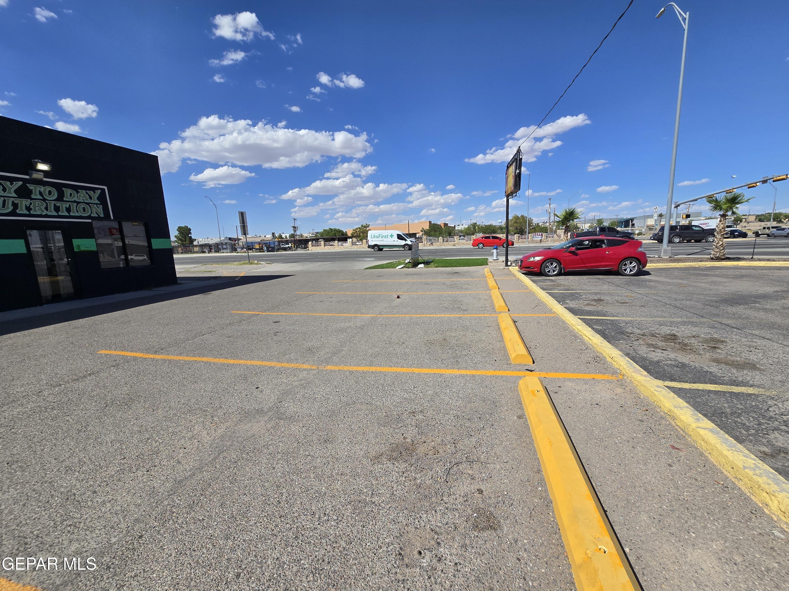 Commercial parking lot with yellow-marked spaces beside a dark storefront and a red car.