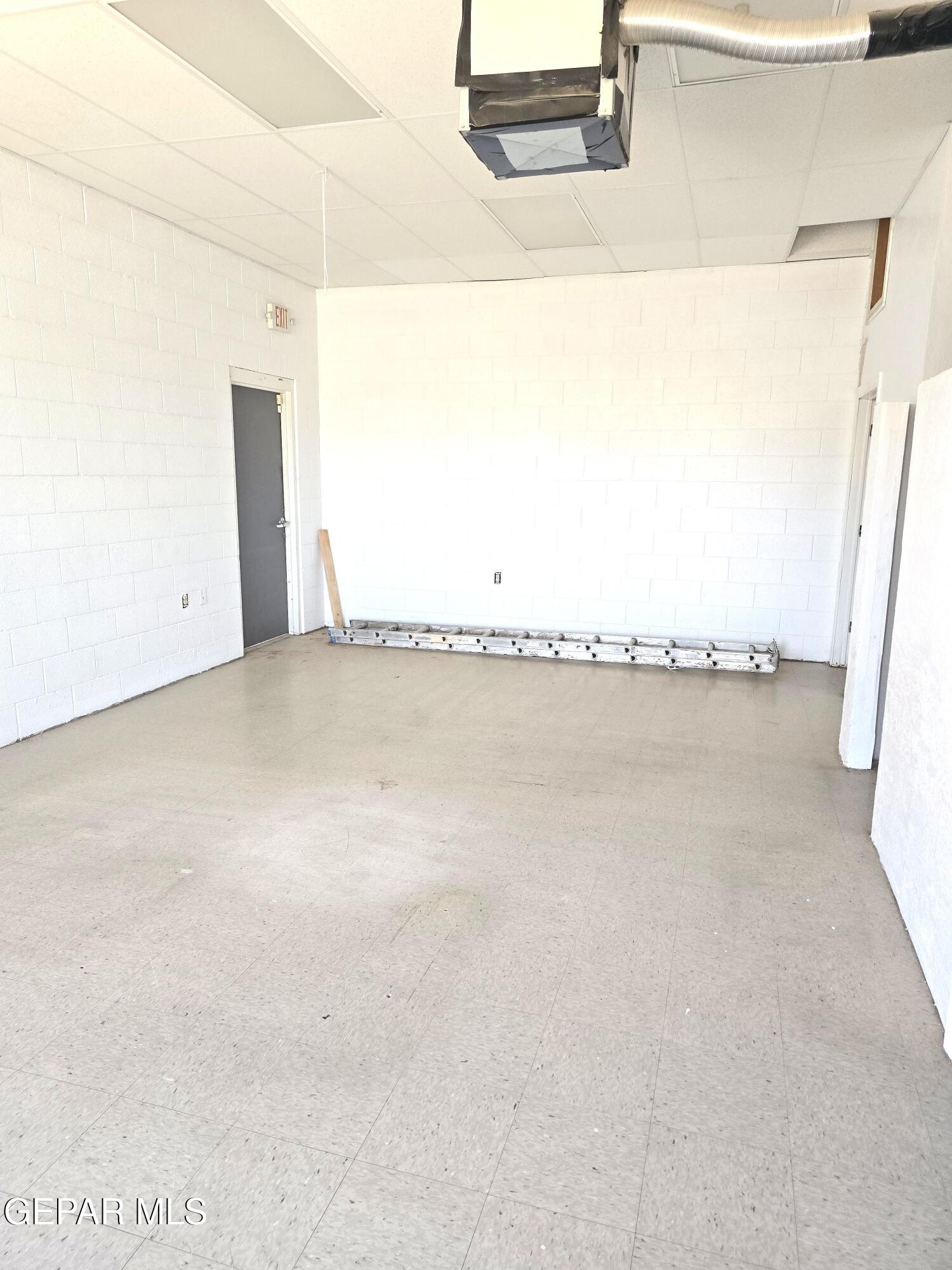 Vacant commercial interior with white block walls, tiled floor, and exposed ceiling ductwork.