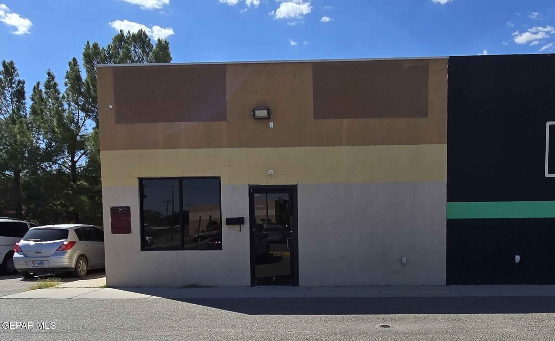 Commercial building exterior with a tan and gray facade, dark entrance, and parked cars.