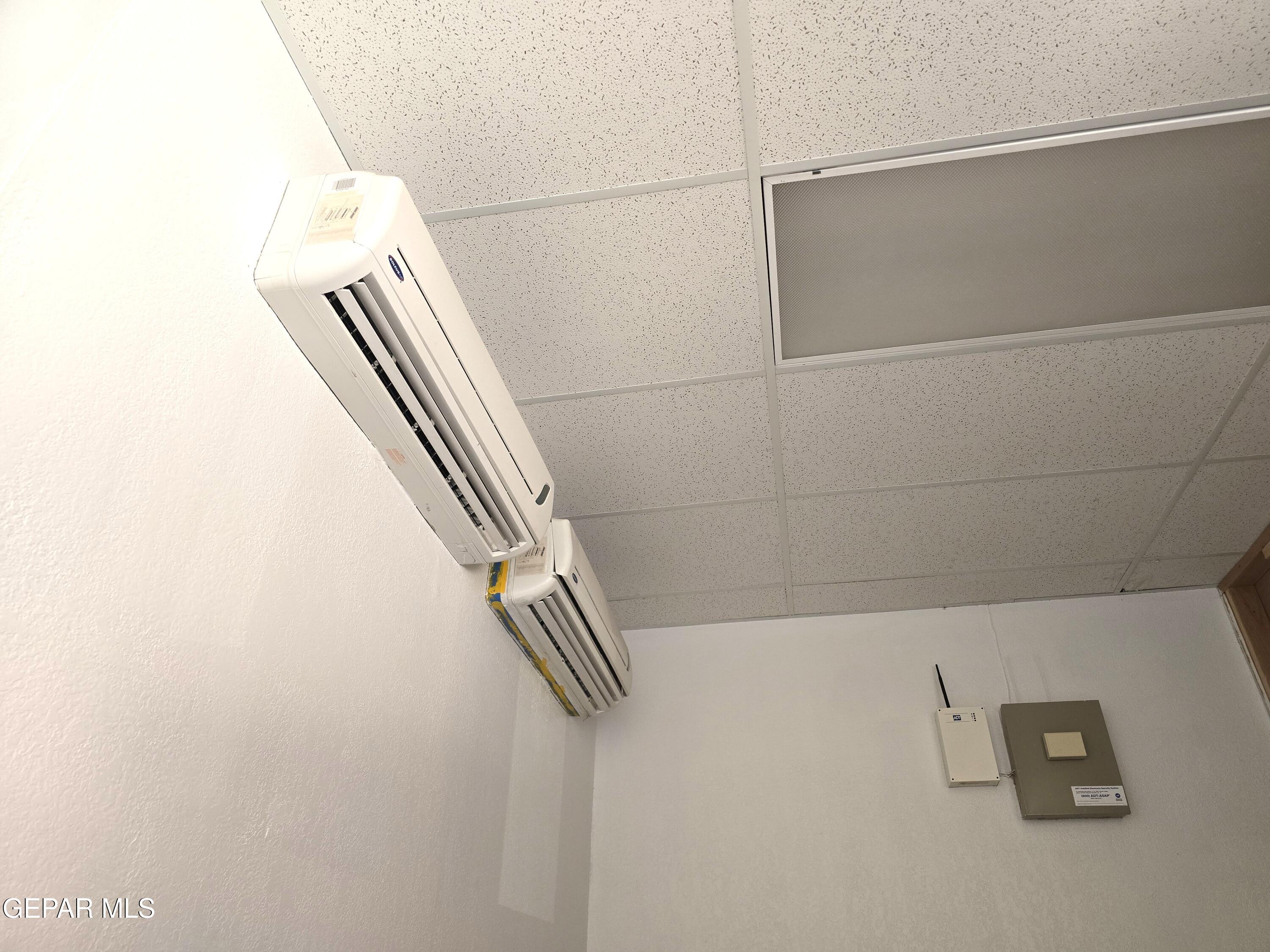 Two wall-mounted air-conditioning units beneath a suspended ceiling, with control panels on the wall.