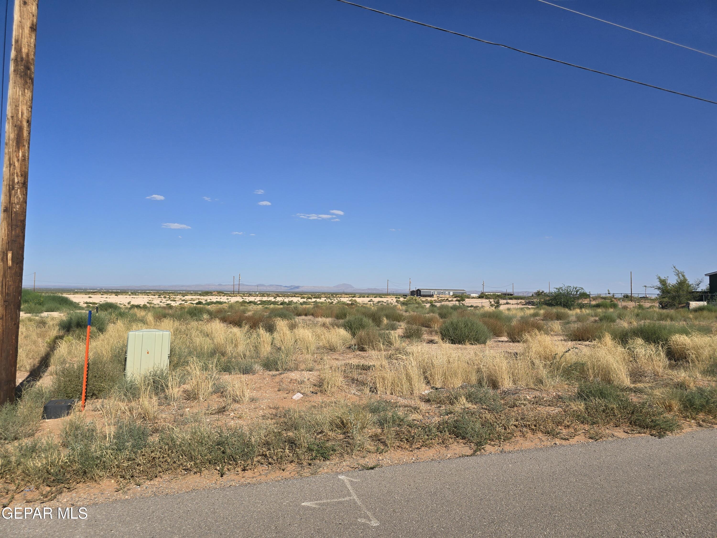Vacant desert lot beside a paved road, with dry grasses, utility lines, and distant hills.
