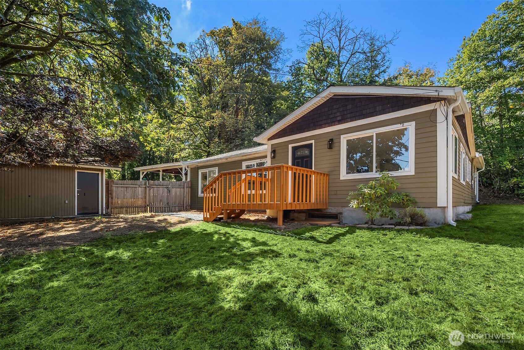 Tan-sided house with a bright orange-railed front porch, lawn, and detached shed among mature trees.