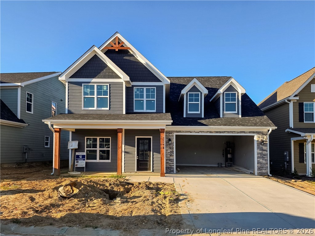 Two-story gray house with a covered porch, stone-accented garage, and unfinished front yard.