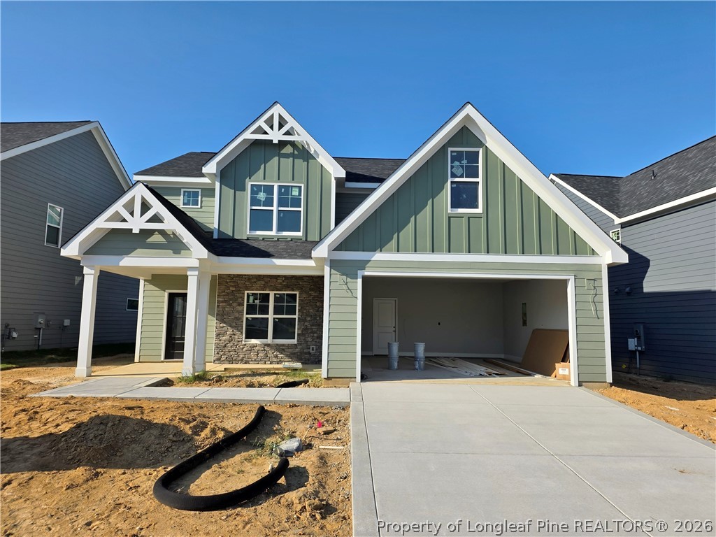 Two-story sage-green home under construction, with white gables, a stone accent wall, and an open garage.