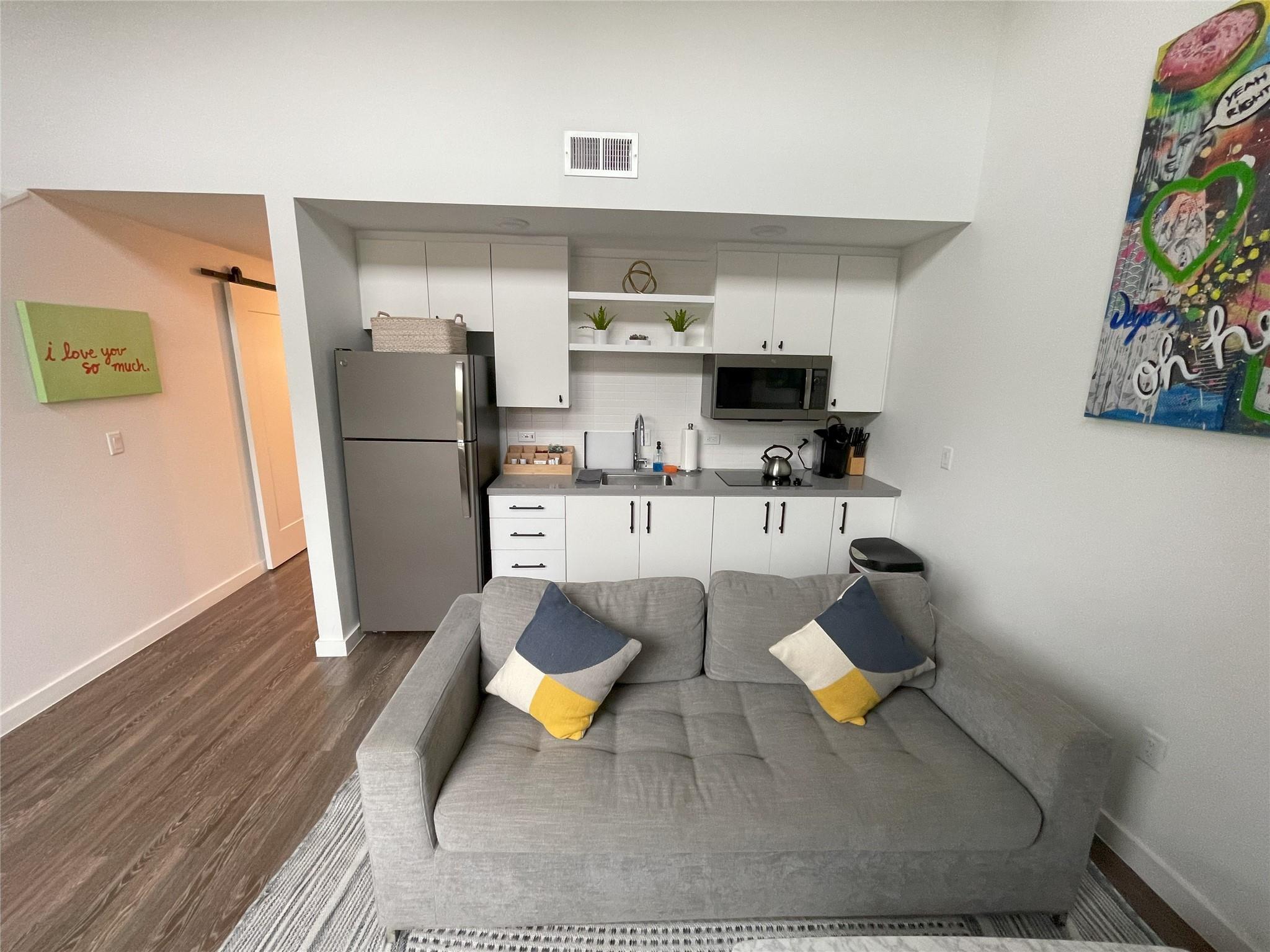 Open-plan living room and kitchen with a gray sofa and compact white-cabinet kitchen.