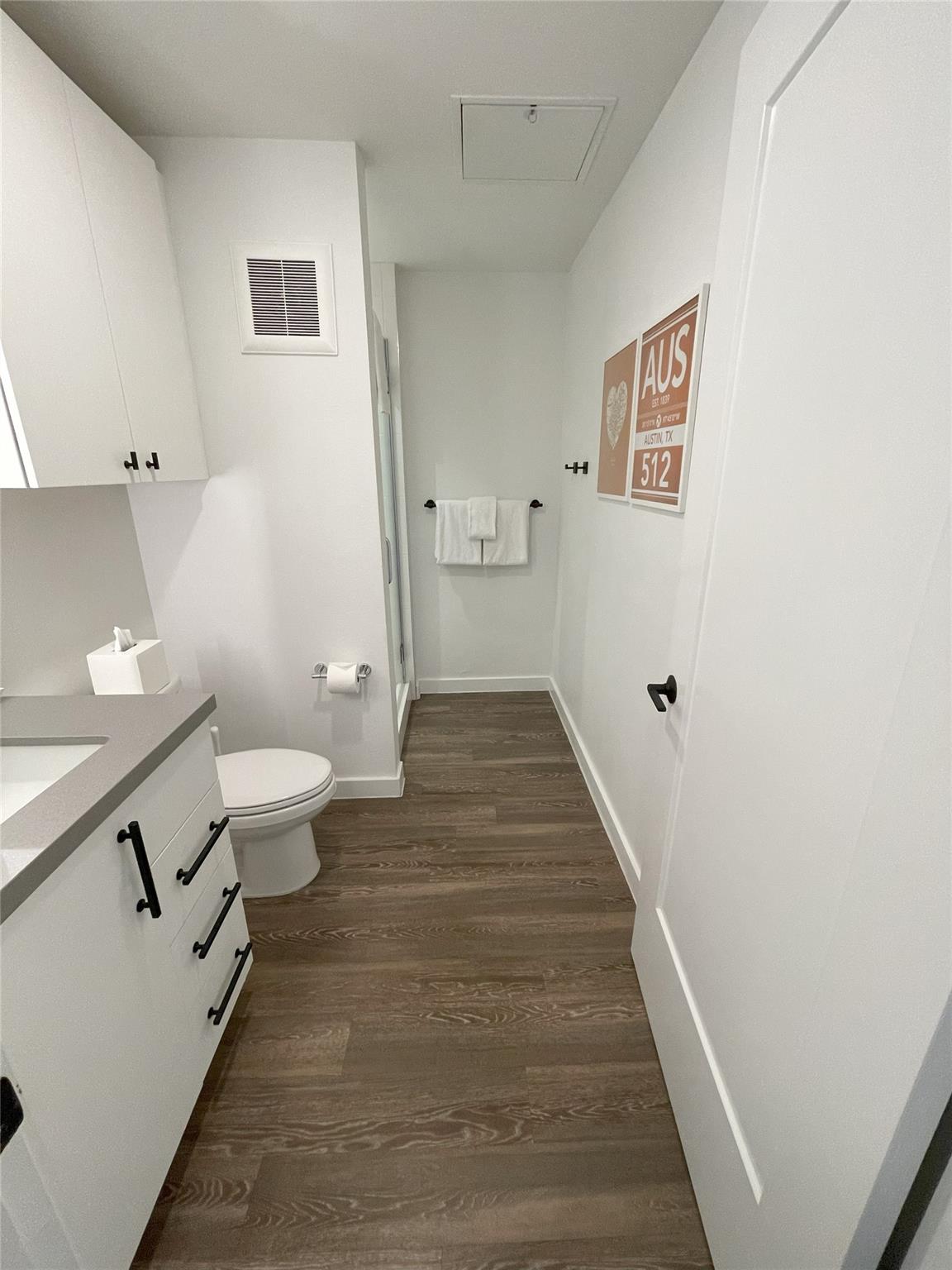Bathroom with a white vanity, glass shower, and brown wood-look flooring.