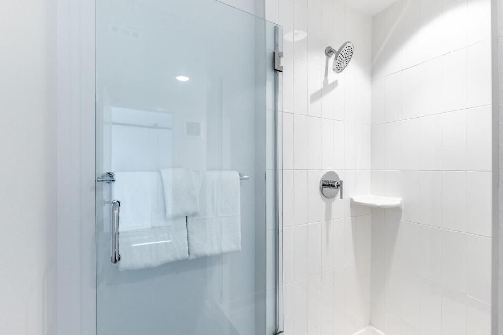 Modern tiled shower with a glass door, rainfall showerhead, and white towels.