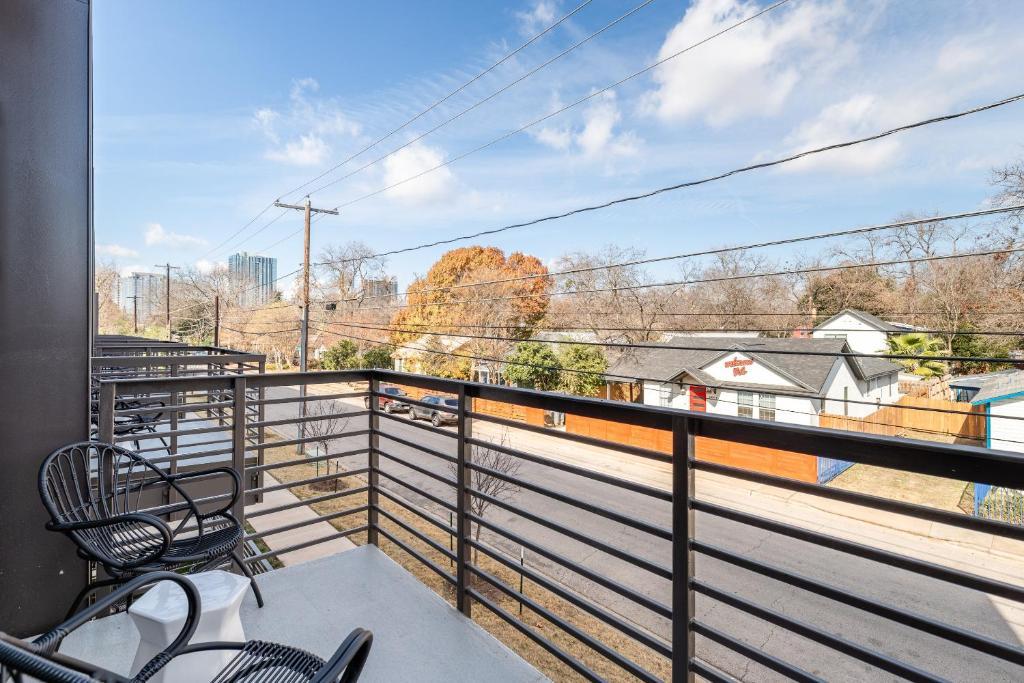 Apartment balcony with black metal railings and chairs overlooking a street and distant buildings.